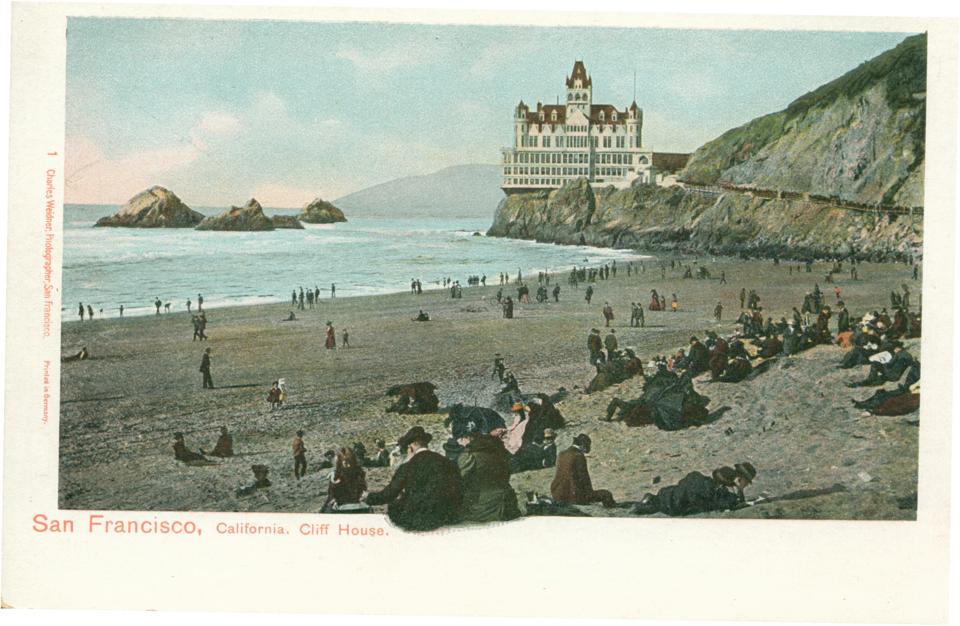 Shows the Cliff House and Seal Rocks, with several individuals on the beach in the foreground.
